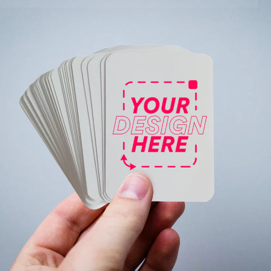 Fan of custom blank playing cards spread on a tabletop with markers and acrylic paints nearby, ready for prototyping.